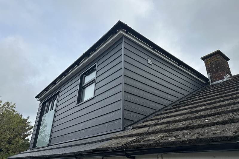 Finished dormer loft conversion at Whyke Close, Chichester: dark grey boarding, a glazed gable end and the brick chimney beside it